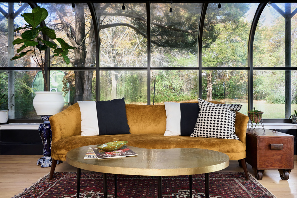 Image of sunroom featuring central couch and coffee table, with large background windows outlooking a yard
