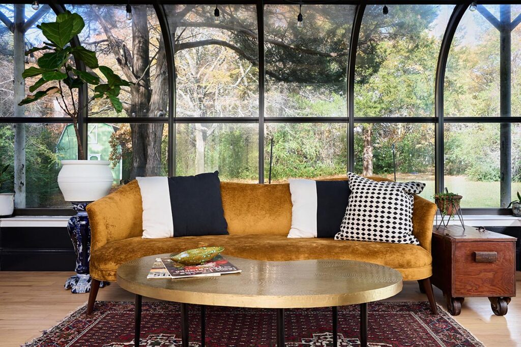 Gold sofa with white and black pillows in front of large full height windows