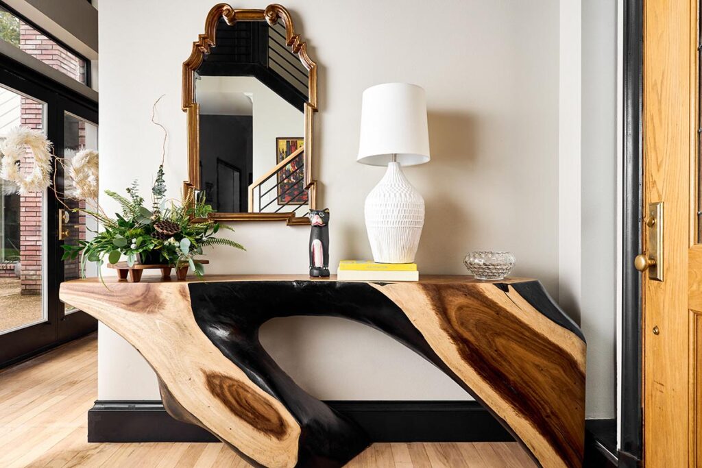 Live-edge wooden table with plant, lamp on top. Gold framed mirror on the wall behind.